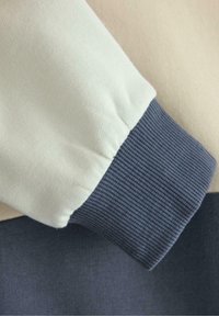 Bluza z blokami kolorów w kremowym i granatowym odcieniu. Posiada ściągacze na rękawach w ciemnym niebieskim, miękką fakturę oraz luźny krój.