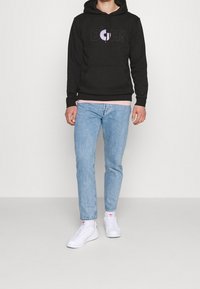 Černá mikina s kapucí s fialovo-bílou grafikou "D'OH!", s klokaní kapsou, nošena přes světle růžové tričko, v kombinaci se světle modrými džíny a bílými teniskami.