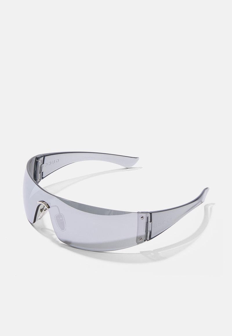 Óculos de sol com uma armação cinza transparente, lentes largas e detalhes em hardware prateado. Apresenta um leve design envolvente para maior cobertura.