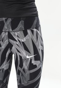 Zwarte sportleggings met een wit abstract geometrisch patroon en een klein wit Nike-logo. Gemaakt van elastisch materiaal voor comfort.