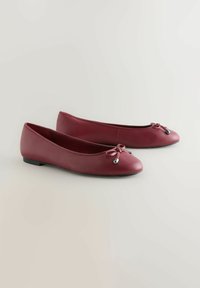 Ballet flats nahkaa tummanpunaisina, pyöreällä varvashuolella, pieni rusetti etupuolella ja litteillä kumipohjilla. Sileä pinta kiiltävällä viimeistelyllä.