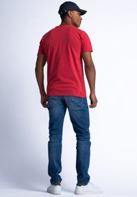 Red short-sleeved t-shirt, cotton material, standard fit, paired with blue denim jeans, and white sneakers, viewed from the back.