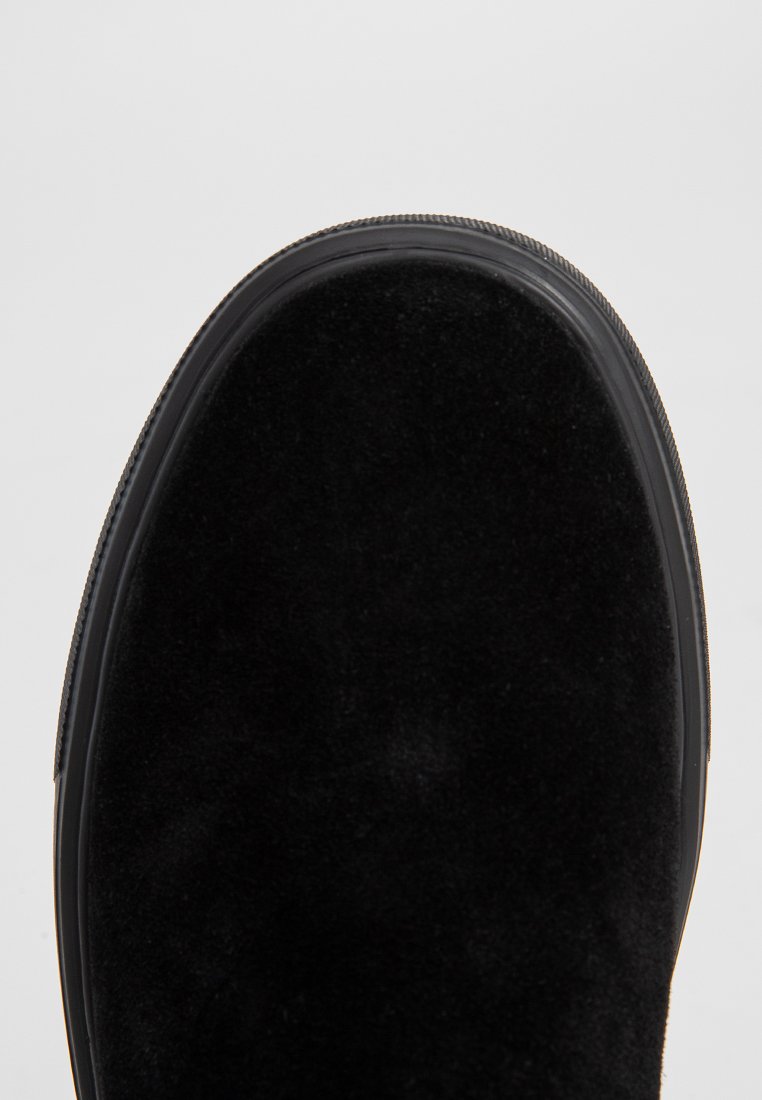 Scarpa nera in suede con punta arrotondata e suola in gomma nera. Presenta una texture liscia e un design minimalista, che mette in risalto il materiale pregiato.