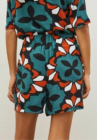 Ensemble court à imprimé floral dans des teintes vives de turquoise, noir, orange et blanc. Comprend une coupe décontractée, une ceinture élastique et des manches courtes.