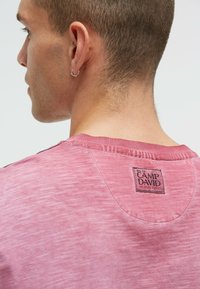 Pink cotton T-shirt with a textured finish, featuring a rounded collar and a stitching detail. Displays a "CAMP DAVID" fabric label on the back.