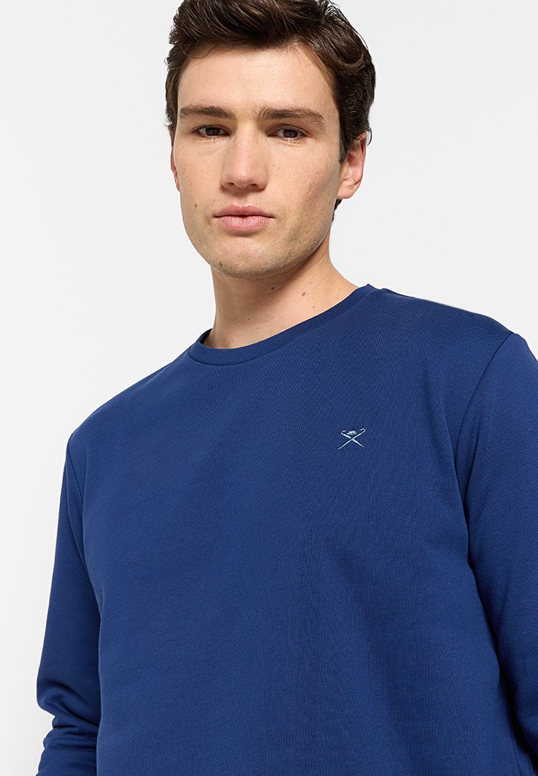 Camiseta de algodón azul de manga larga con cuello redondo y un pequeño logo bordado en el pecho. Textura suave con un diseño ajustado.