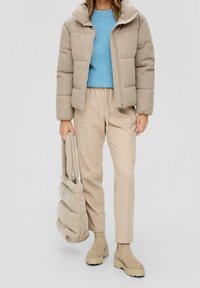 Beige péřová bunda s prošívanými částmi, modrý pletený svetr, béžové kalhoty, taupe kotníkové boty a měkká béžová taška.
