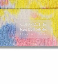 Tkanina dzianinowa z wzorem tie-dye w kolorach żółtym, niebieskim i różowym. Posiada wyraźną metkę z napisem "Oracle Red Bull Racing" w kolorze białym.