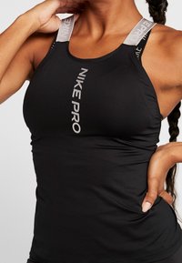 Zwarte Nike Pro tanktop met grijze schouderbanden. Heeft een strak ontwerp, een aansluitende pasvorm en een gedrukt logo aan de voorkant. Gladde textuur.