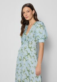 Jasnoniebieska sukienka w kwiaty z zielonymi wzorami roślinnymi, krótkimi bufkami i głębokim dekoltem w kształcie V. Gładki materiał z luźnym krojem.