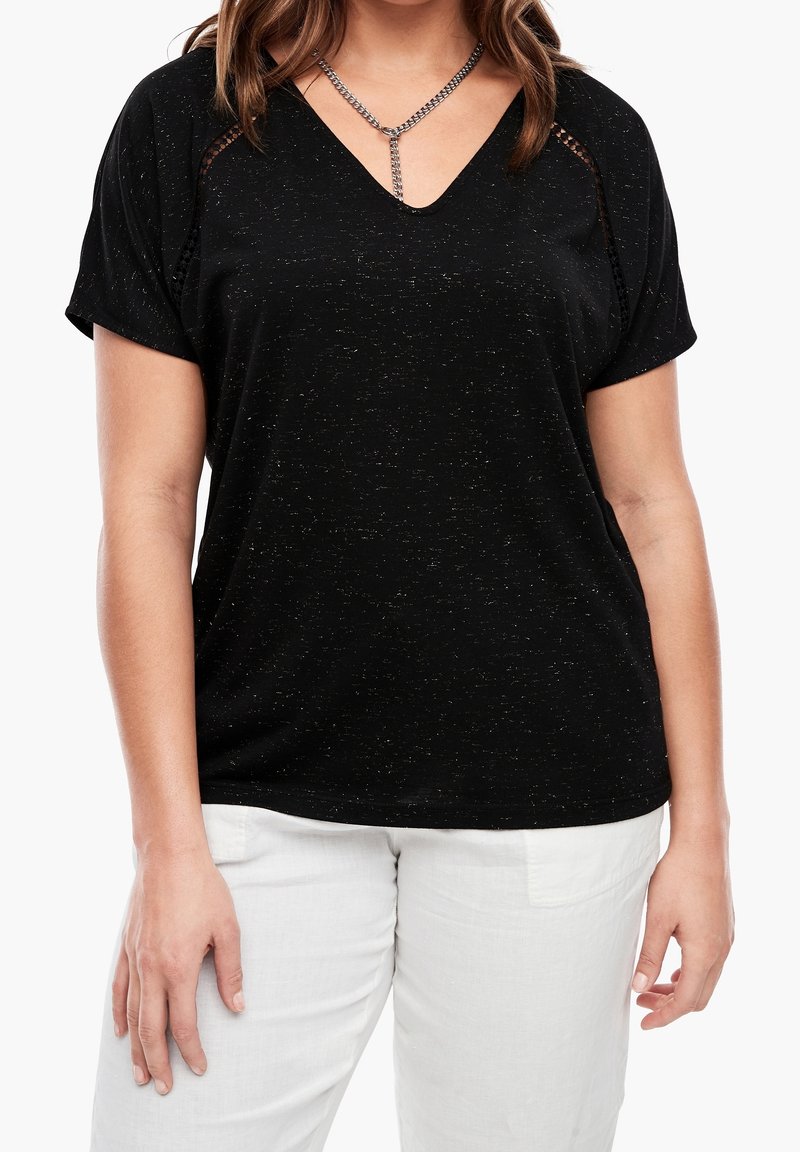Haut noir à manches courtes avec col en V, finition texturée et accent décoratif en chaîne. Associé à un pantalon en lin blanc pour un contraste.