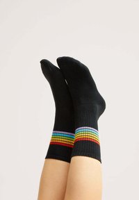Schwarze gerippte Socken mit einem mehrfarbigen gestreiften Muster am Bündchen, das lebendige horizontale Linien in Rot, Orange, Gelb, Grün und Blau zeigt.