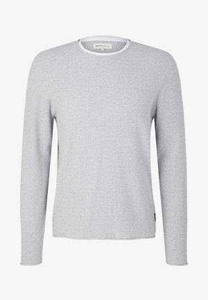 Giacca camicia in misto lana grigia con due tasche sul petto, indossata sopra una camicia bianca a maniche lunghe con texture, abbinata a jeans grigi strappati e sneakers bianche.