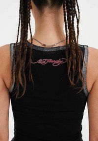 Top nero senza maniche con accenti metallici argento, caratterizzato da un design aderente e un logo ricamato rosso "Ed Hardy" sulla parte posteriore. Tessuto texturizzato.