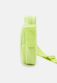 Borsa a tracolla verde chiaro con una texture morbida in tessuto, dotata di chiusura con cerniera e tracolla regolabile. Include una linguetta in Velcro per una chiusura sicura.