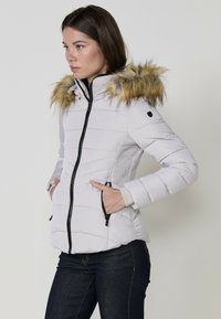 Világosszürke steppelt dzseki, prémes kapucnival, fekete cipzárral, oldalzsebekkel és texturált részletekkel az oldalán. Sima külső anyag.