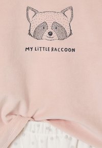 Light pink t-shirt with a raccoon graphic and the text "MY LITTLE RACCOON." Soft fabric with a smooth texture and curved hem.