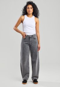 Gray high-waisted jeans with a relaxed fit, featuring stitching details and pockets. Paired with a white sleeveless top and black sneakers.
