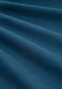 Donkerblauwe stof met een gladde textuur, zachtgevouwen, met subtiele schaduwen en diepte in de plooien. Geen patronen of hardware zichtbaar.