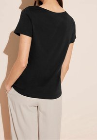Černé tričko s krátkým rukávem vyrobené z měkké bavlny, s kulatým výstřihem a uvolněným střihem, zobrazené zezadu s hladkou texturou.