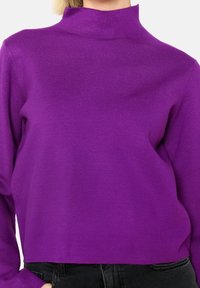 Suéter morado de cuello alto hecho de una suave tela de punto. Presenta mangas largas y una silueta ajustada. Terminación limpia a la altura de la cintura.
