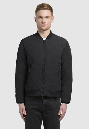 Chaqueta bomber acolchada negra con cierre de cremallera, puños y cinturilla acanalados, con bolsillos laterales y una textura suave.