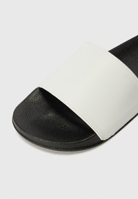 Sort og hvid slidesandal med en struktureret sort sål og et glat hvidt overbånd. Åben tå-design, ingen metaldele eller dekorationer.