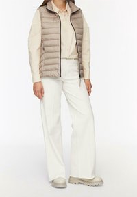 Beżowa pikowana kamizelka z zapięciem na zamek, kremowa koszula na guziki, szerokie spodnie w kolorze ecru oraz beżowe botki na masywnej podeszwie. Minimalistyczny design.