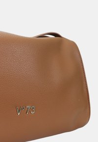 Bolso de cuero marrón con textura y un acabado suave. Presenta un logo dorado "V°73" en la parte inferior izquierda, forma profunda y un asa resistente.
