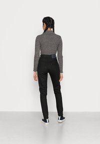 Vaqueros de talle alto negros combinados con un suéter de cuello alto de punto gris. El conjunto presenta un diseño simple, con una textura suave y una silueta ajustada.