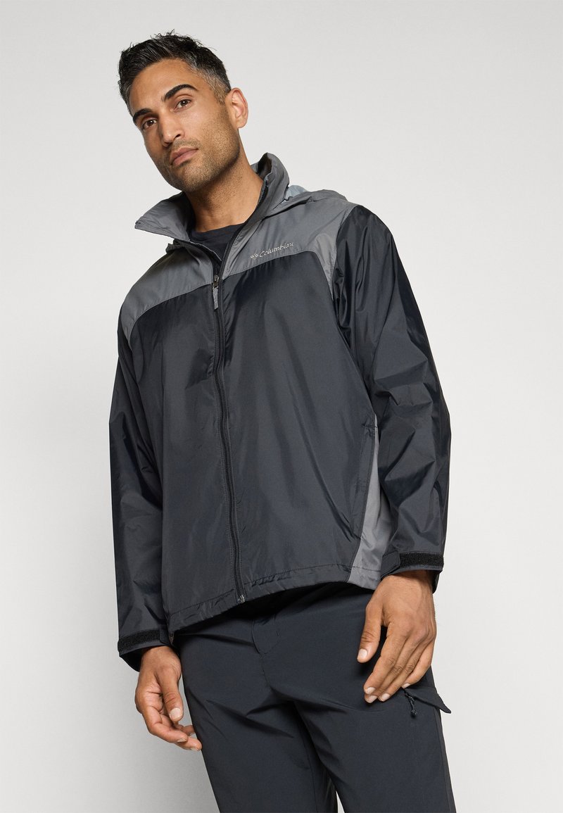 Chaqueta impermeable negra y gris con cierre de cremallera en el frente, cuello alto y mangas largas. Presenta un logo en el hombro izquierdo y puños elásticos.