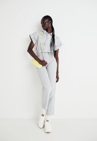 Světle šedý denimový overal s krátkými rukávy, širokými nohavicemi a předními knoflíky. Užitý s bílými teniskami a malou žlutou křížovou taškou.