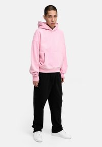 Light pink hooded sweatshirt with a front pocket, paired with black joggers and white sneakers. Soft texture, casual fit, and simple design.