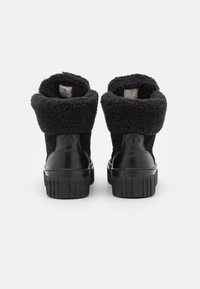 Botas negras hasta el tobillo con un exterior de lana suave y texturizada y acentos de charol brillante. Suelas de goma gruesas y estriadas y puños que se pueden doblar.