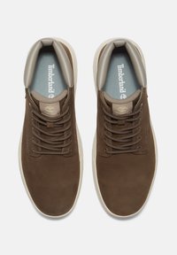 Hnědé kožené tenisky s hladkým svrškem, kulatou špičkou, béžovými detaily a tmavými šňůrkami. Branding Timberland na jazyku a stélce.