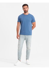 Modré bavlněné tričko s krátkým rukávem a kulatým výstřihem, spárované s lehkými potrhanými džíny a bílými teniskami. Jednoduchý design a uvolněný střih.