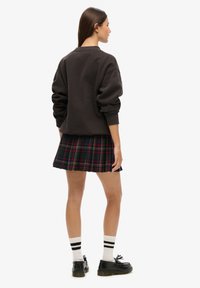 Donkergrijze sweatshirt met verlaagde schouders, gecombineerd met een geplooide groene ruitjesrok met rode en gele lijnen. Zwarte schoenen en gestreepte sokken.