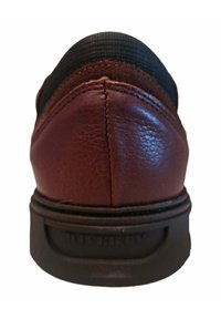 Zapato de cuero burdeos con textura suave, suela de goma negra y detalles de costura visibles en la parte posterior. Sutil logo de la marca en el talón.