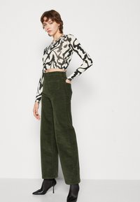 Zwart-witte abstracte patroon lange mouw crop top, gecombineerd met hooggewaisted, wijde olijfgroene corduroy broeken en zwarte haklaarzen.