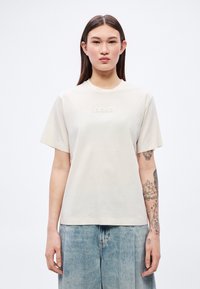 Ανοιχτό μπεζ κοντομάνικη μπλούζα κατασκευασμένη από μαλακό βαμβάκι. Διαθέτει υφασμένo λογότυπο «BOSS» στο κέντρο του στήθους. Απλός, χαλαρός σχεδιασμός.