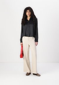 Chemise noire en satin à boutons, pantalon large beige en lin, sac rouge et chaussures imprimé léopard. Texture lisse, coupe décontractée et couleurs accrocheuses.