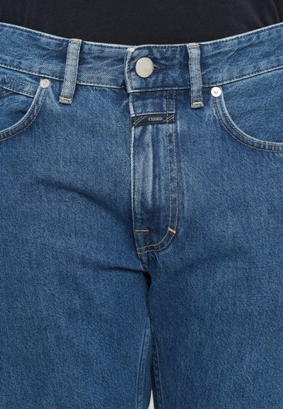 Blue denim jeans with a classic five-pocket design, high waist, and visible stitching. Features a metal button and branded label at the waistband.