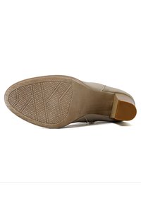La suola di una scarpa con tacco beige presenta una superficie in gomma testurizzata per una migliore aderenza, una forma a punta arrotondata e un accento marrone sul tacco.