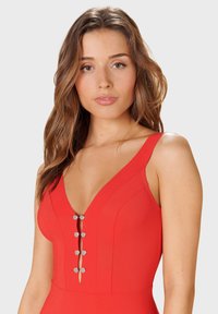 Červené plavky s hlbokým výstrihom do V, širokými ramienkami a piatimi kruhovými kovovými gombíkmi pozdĺž prednej časti. Hladká, textúrovaná tkanina.