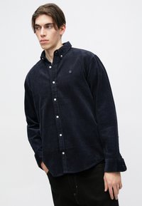 Ναυτικό κορδερο shirt με γιακά που κουμπώνει, μακριά μανίκια και διακριτό λογότυπο στο στήθος. Διαθέτει λευκούς κουμπιά και υφασμάτινη υφή.