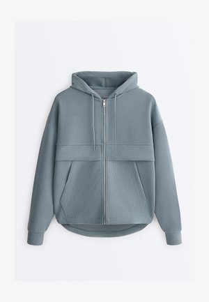 Világoskék bordázott cipzáras kapucnis pulóver elülső zsebekkel, húzózsinórokkal és enyhén ívelt szegéllyel.