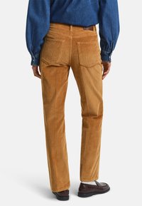 Bruine corduroy broek met een rechte pasvorm, voorzien van twee achterzakken en een subtiele ribbeltextuur. Gecombineerd met donkere schoenen.