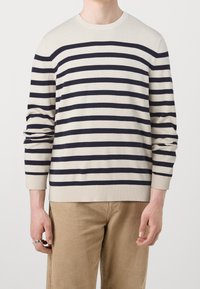 Maglione a righe realizzato in tessuto morbido, con righe orizzontali blu navy su uno sfondo beige. I polsini e l'orlo a coste accentuano il design.