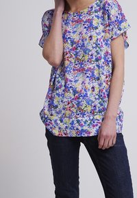 Bloemmotief top met een multicolorpatroon van blauwe, gele en roze bloemen op een lichte stof, met een relaxte pasvorm en korte mouwen.