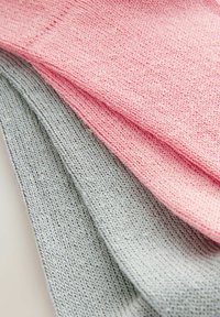 Tre strikkede sokker stablet: en lys pink, en lys grå. Materialet er blødt, med et tekstureret mønster og ensartet stræk.